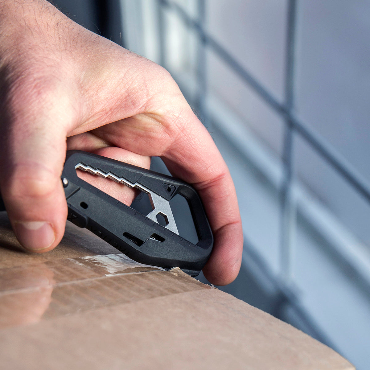 Closeup of a person using the m100 multitool to cut open a package